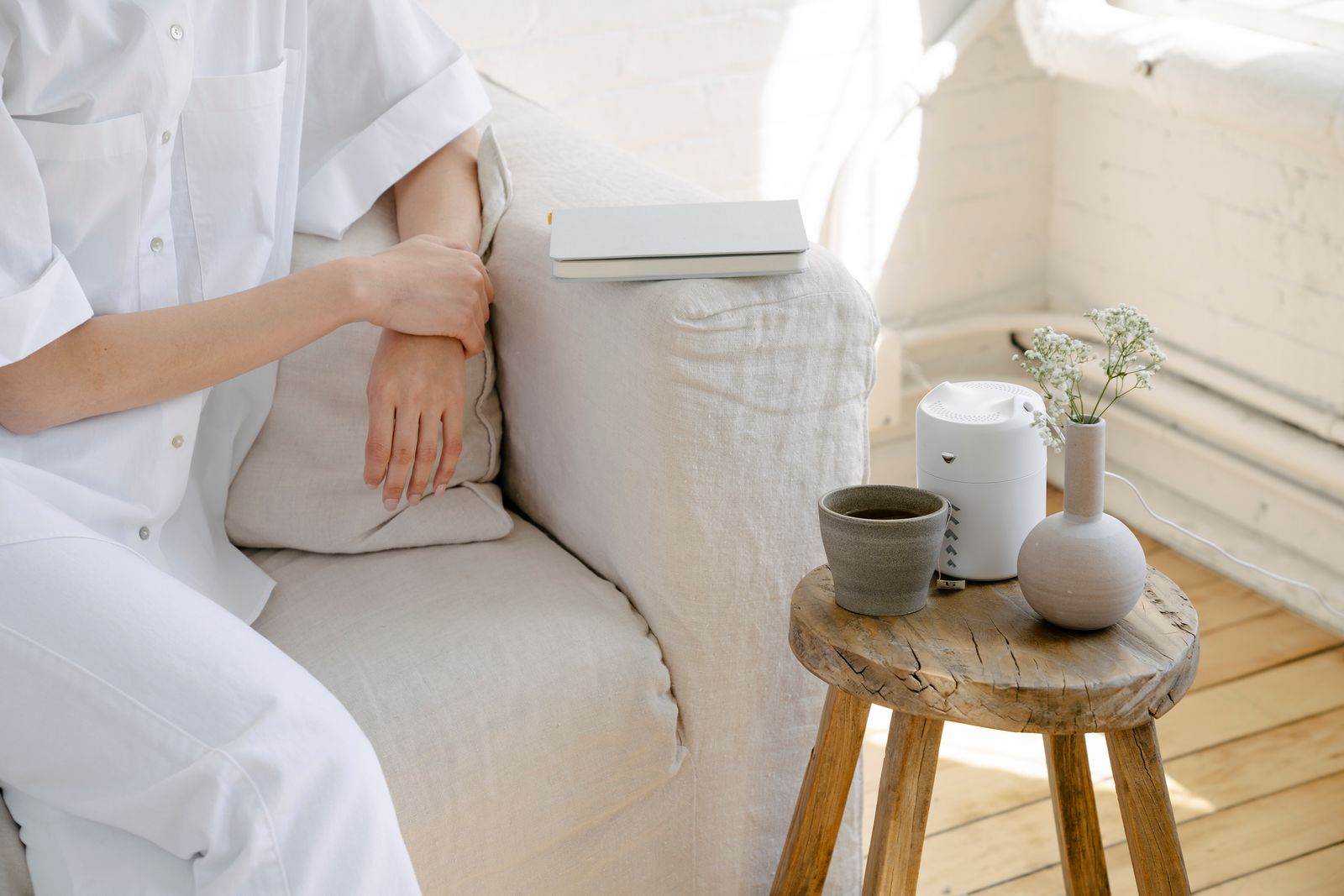 Small white humidifier on a wooden stool beside a sofa in a bright, cozy room