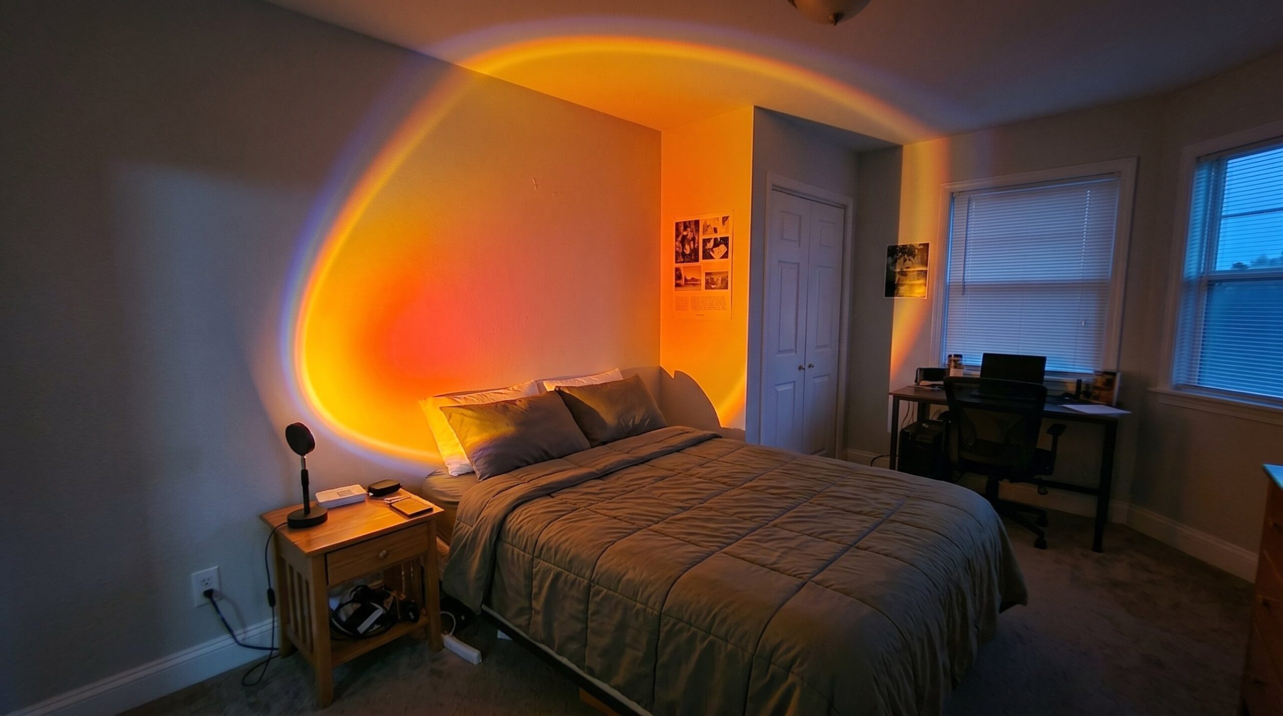 A sunset lamp on a bedside table casting a glowing arc of orange, red and violet light across the bedroom wall